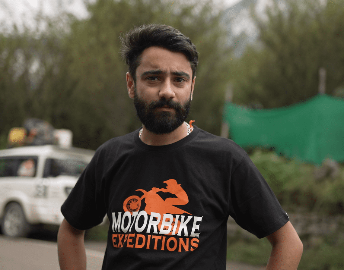 Motorbike expedition mechanic Pranav standing confidently in outdoor setting with vehicles in the background.