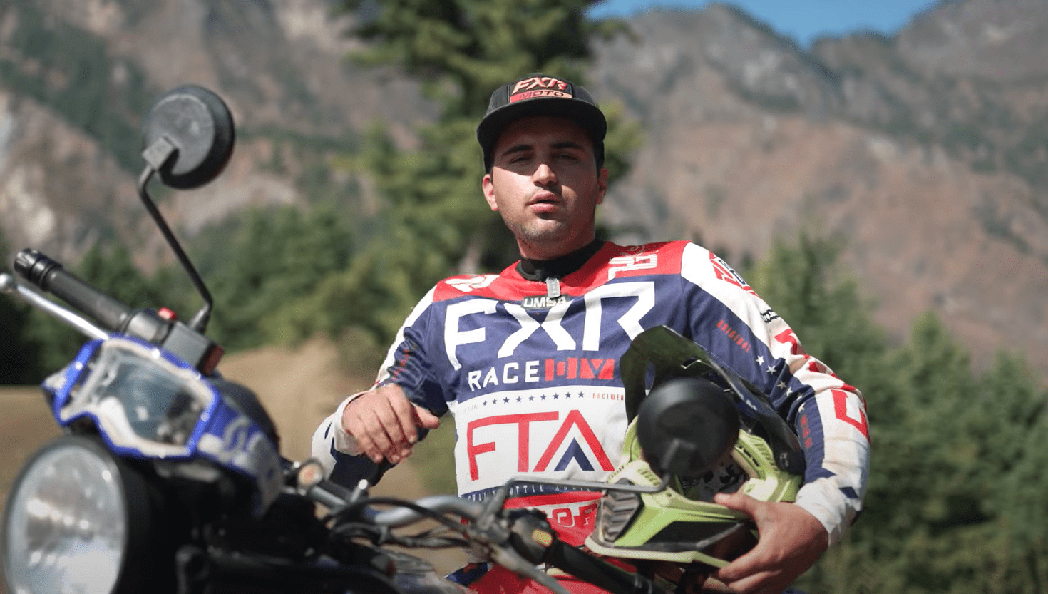 Our Tour Guide and Rally rider Nitesh in FXR gear with off-road motorbike in front of mountain landscape, illustrating the thrill of motorcycle expeditions and professional riding.