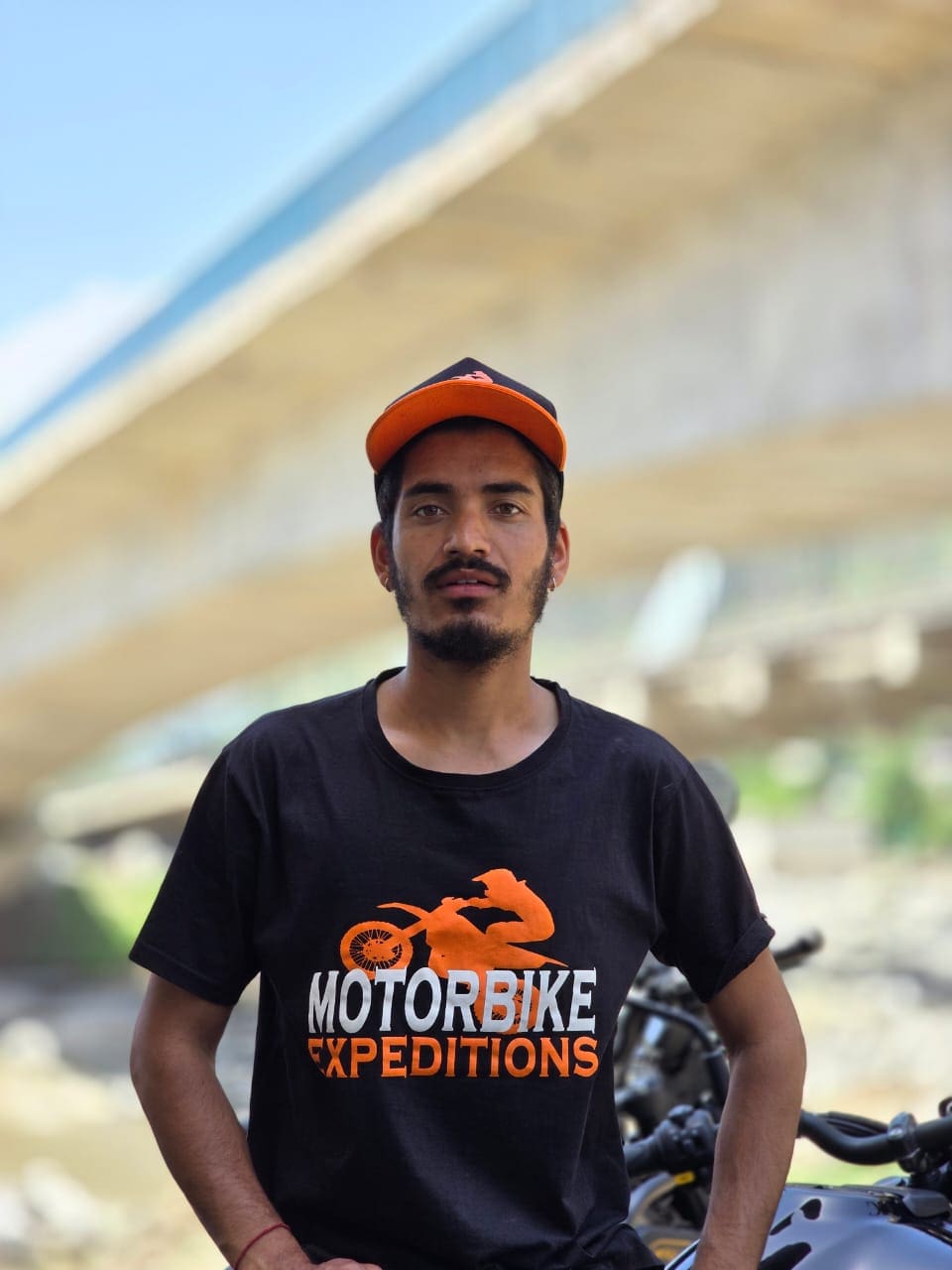 Rahul Thakur, main expeditions guide and gurage manager at Motorbike Expeditions Ltd, wearing a black t-shirt and orange cap, standing next to a motorbike.