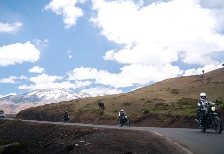 Riders on the Spiti Valley motorbike expedition cruising along winding mountain roads with stunning views of snow-capped peaks and clear blue skies.