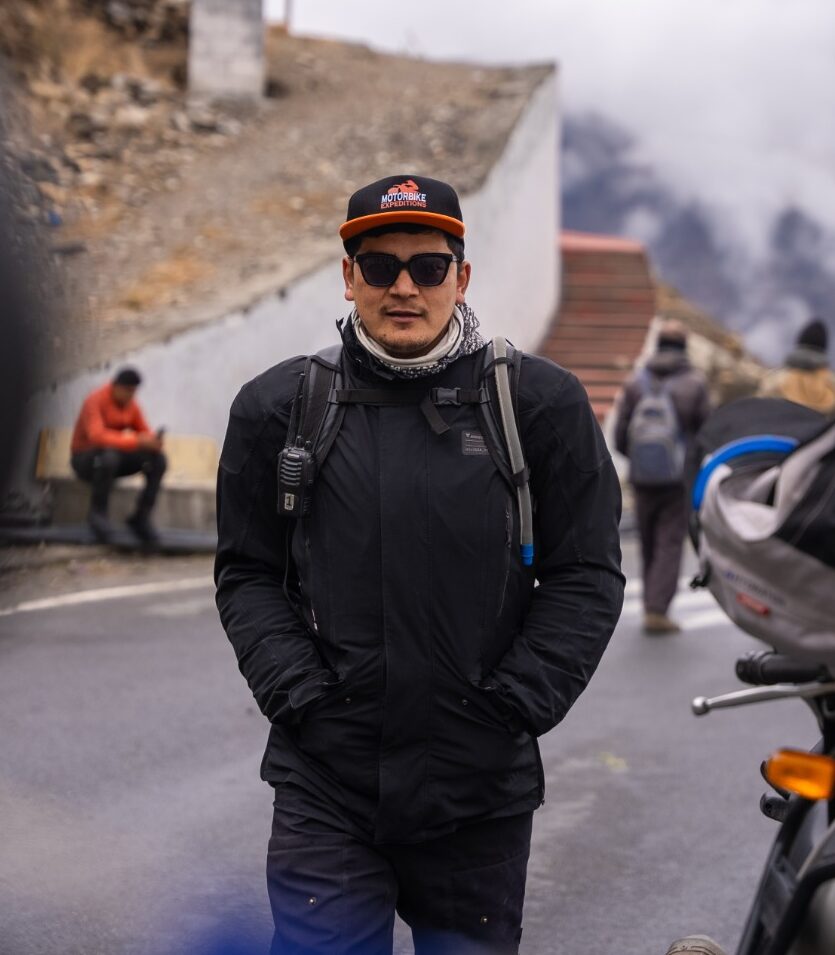 Expedition guide Deepak in the Himalayas wearing black winter clothing and a Motor Expedition cap.