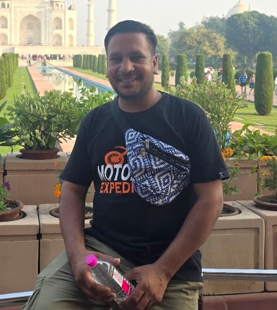 Mechanic from Motor Expedition sitting in front of the Taj Mahal garden, holding a water bottle.