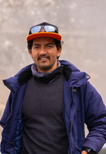 Nitesh, backup driver for Motorbike Expeditions, wearing a blue jacket and cap in a mountain setting.