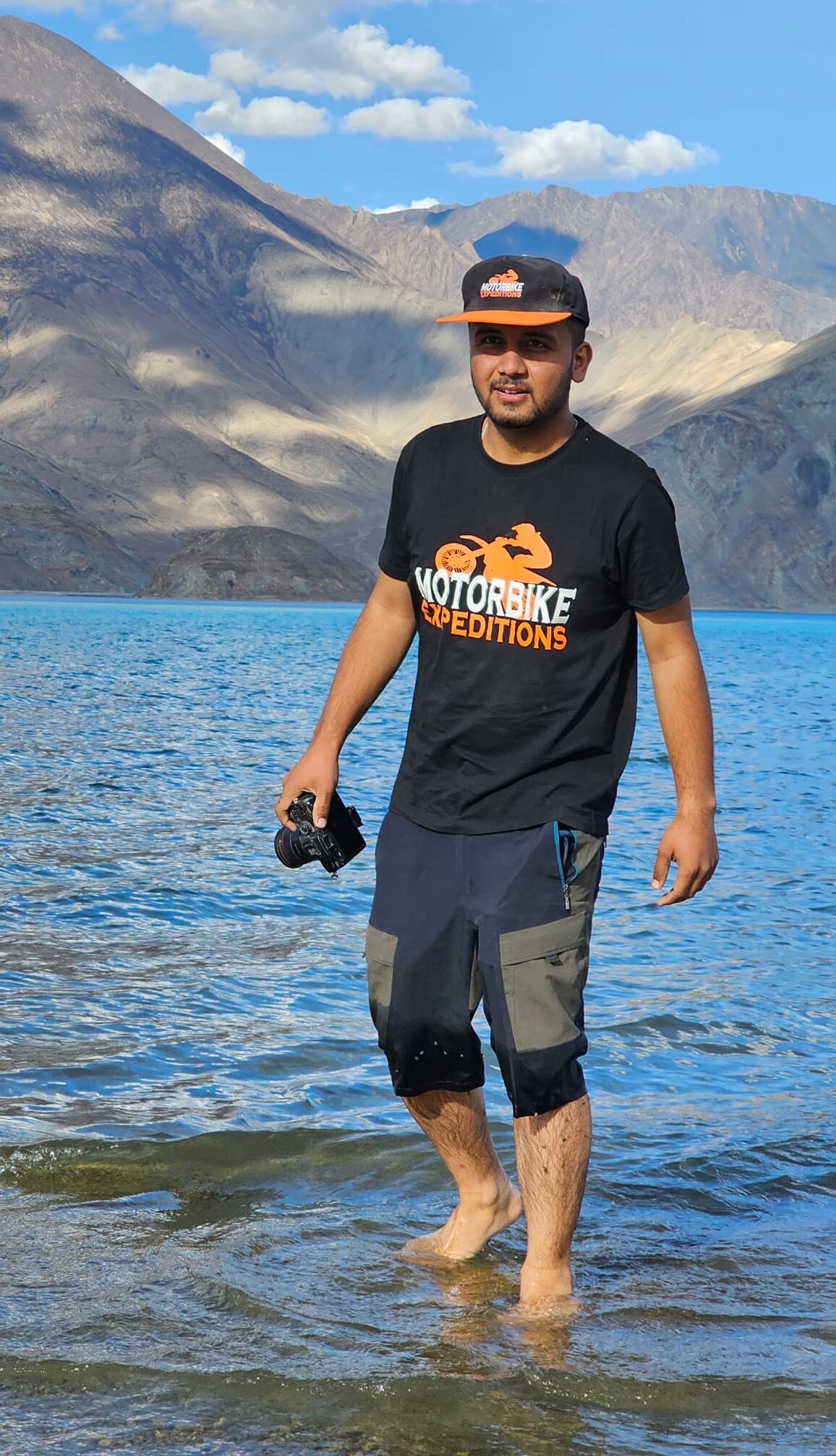 Sam, videographer for Motorbike Expeditions, standing in the water at Pangong Lake with mountains in the background.